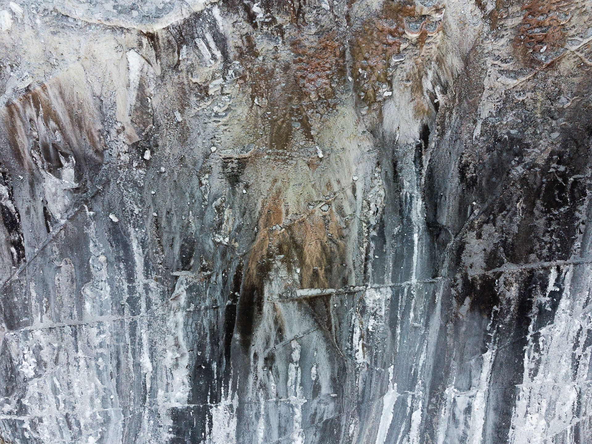 Abstract weathered rock or concrete wall with gray, white, and brown streaks and texture