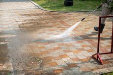 Person pressure-washing a brick patio with a spray wand