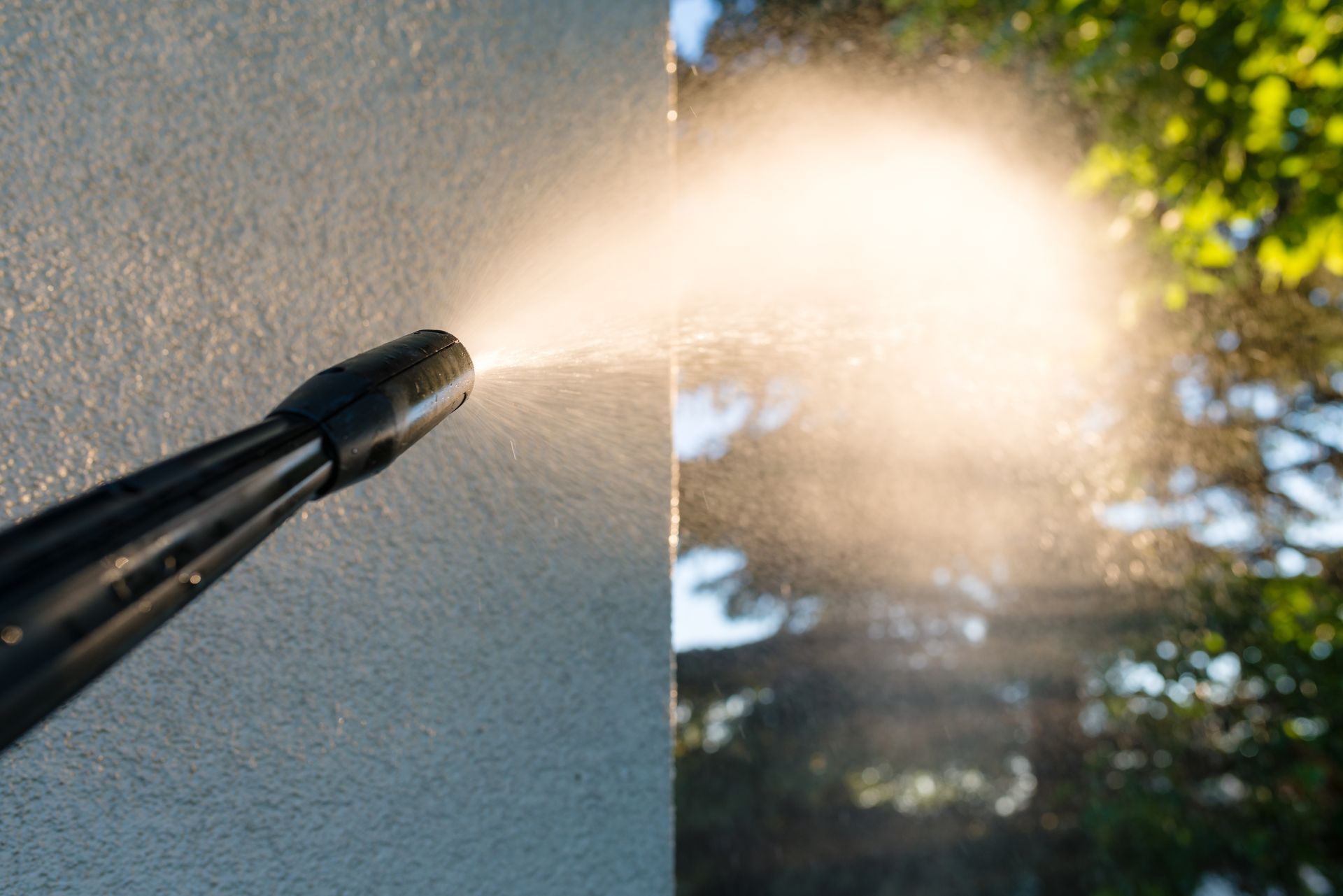 Pressure washer nozzle spraying water, with a cleaned wall on the left and dirty surface on the right