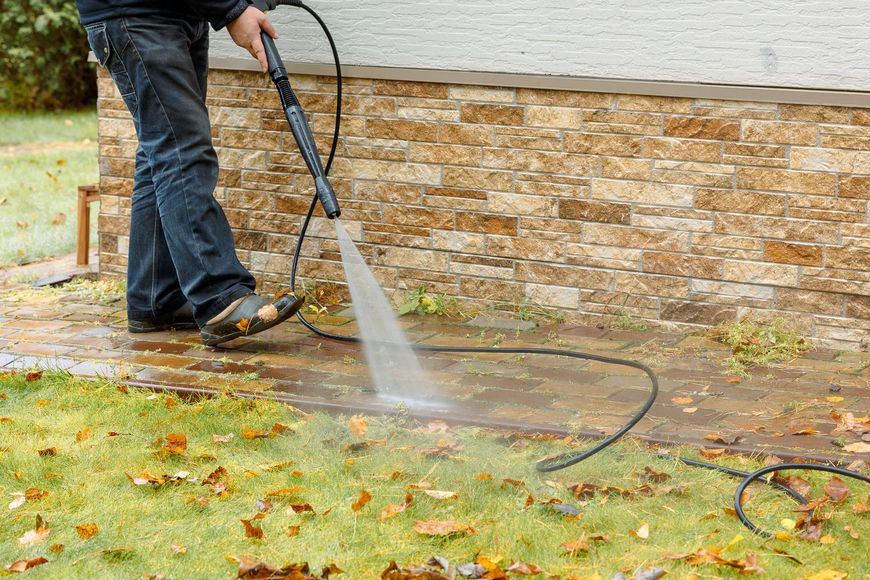 Person pressure-washing a stone wall and pavement in a yard