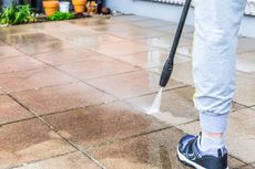 Person pressure washing a wet patio with a black sprayer wand.