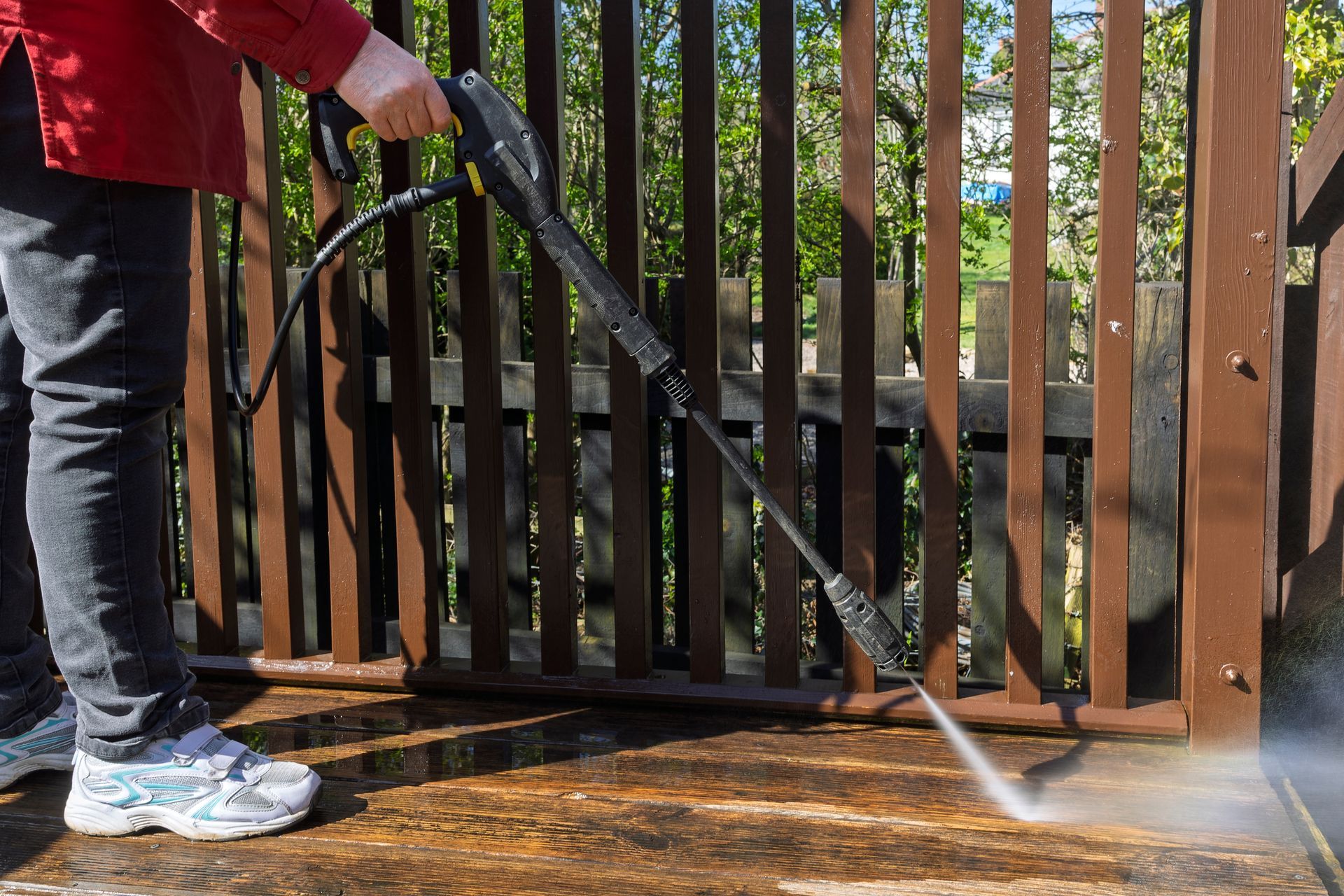 Person pressure-washing a wooden deck with a black hose and spray wand