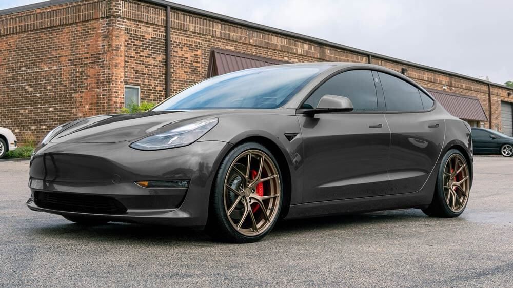 A tesla model 3 is parked in front of a brick building.