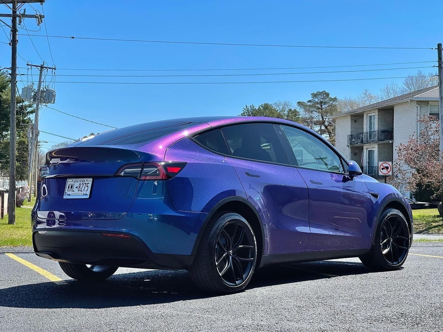 A purple tesla model y is parked on the side of the road.