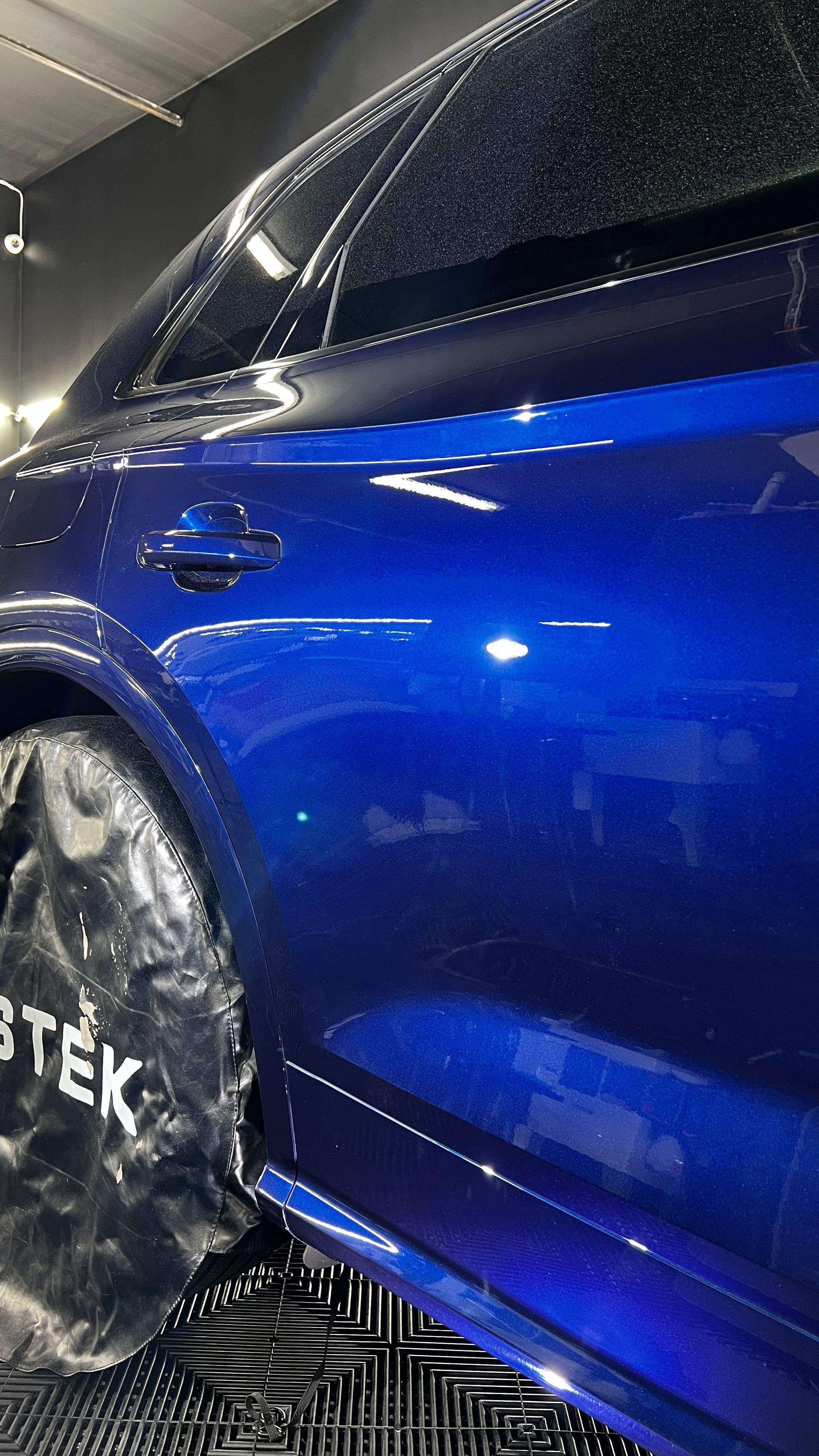 A blue car is sitting on top of a black mat in a garage.