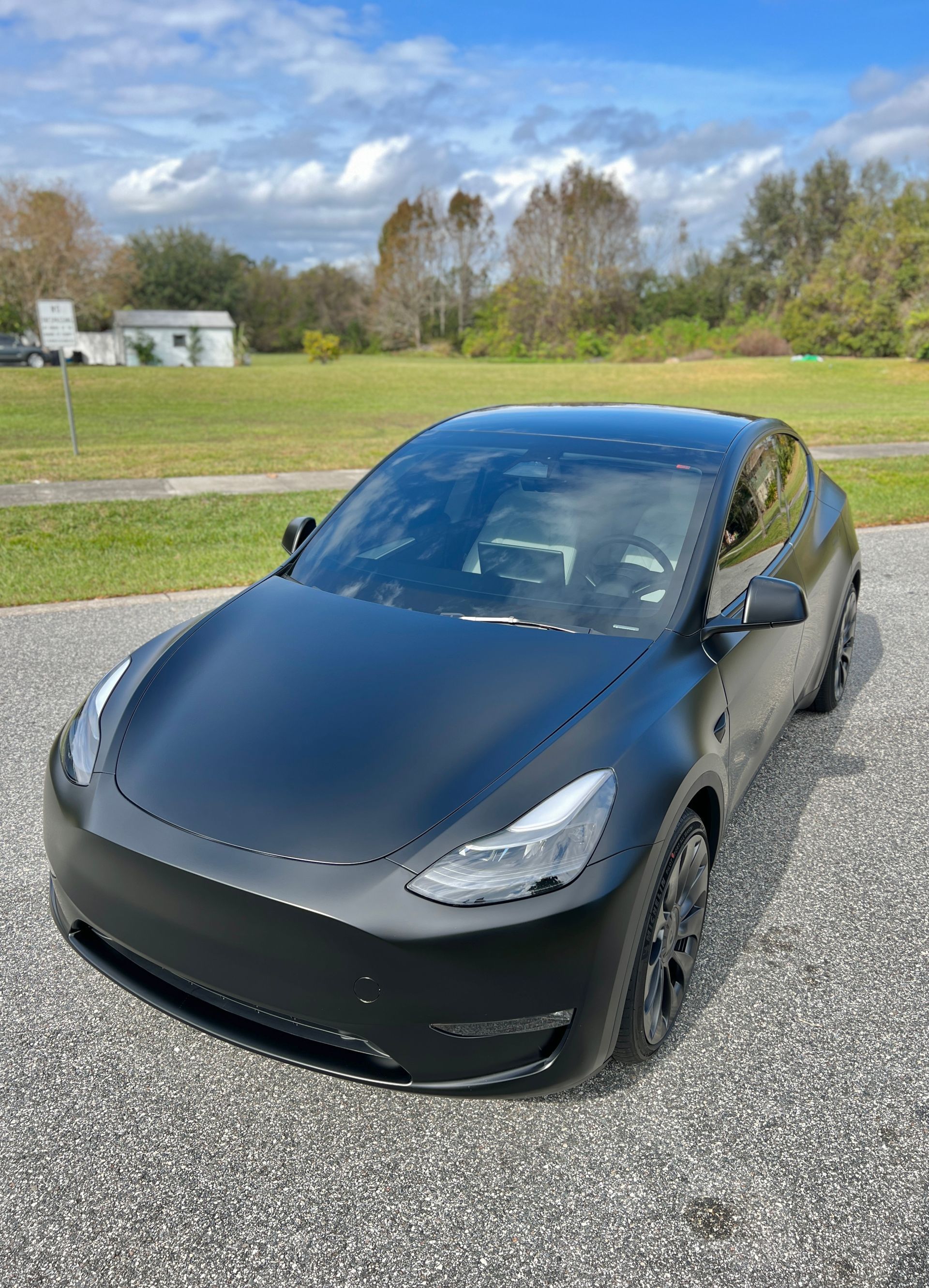 A black tesla model y is parked on a gravel road.