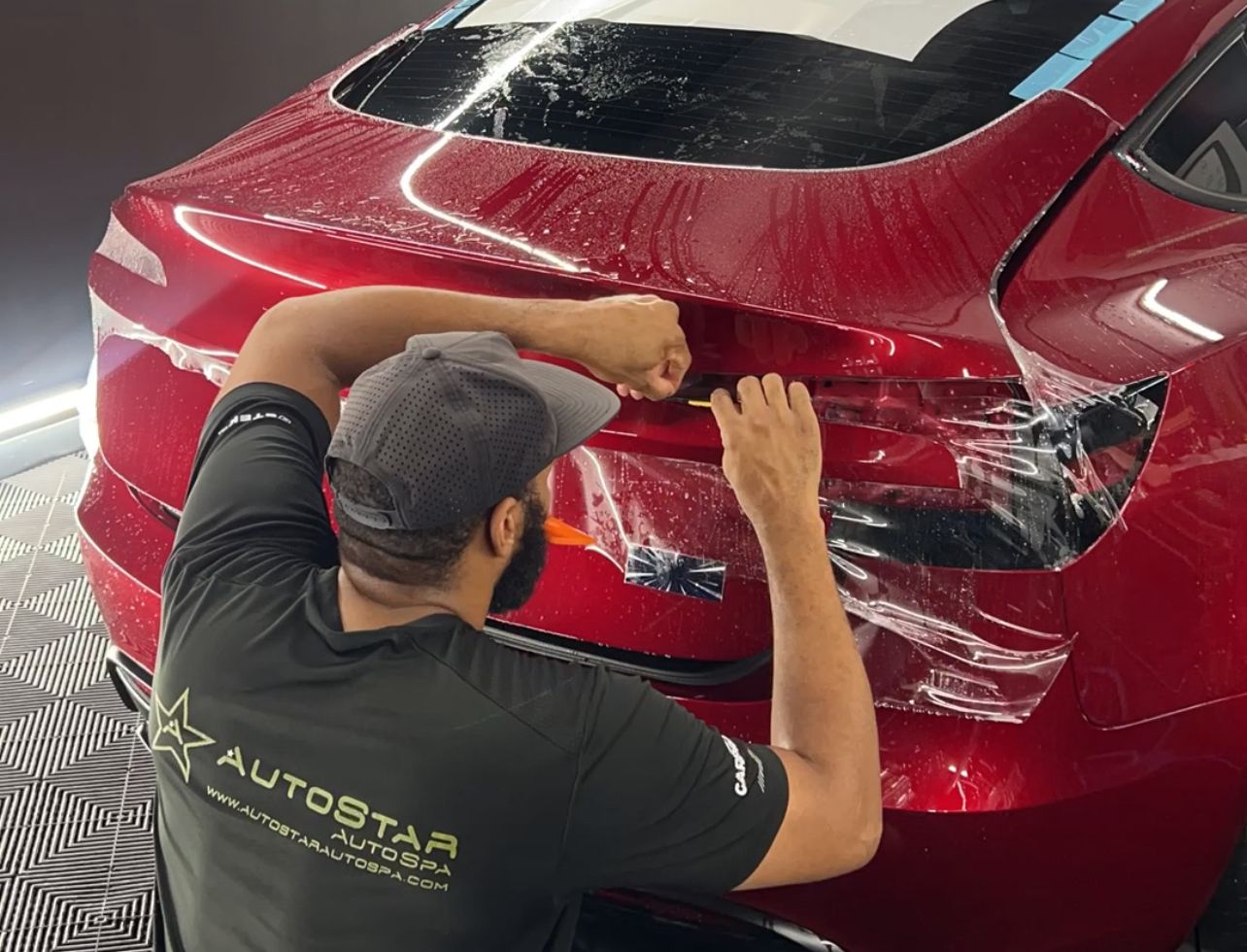 A man is wrapping a red car with paint protection film