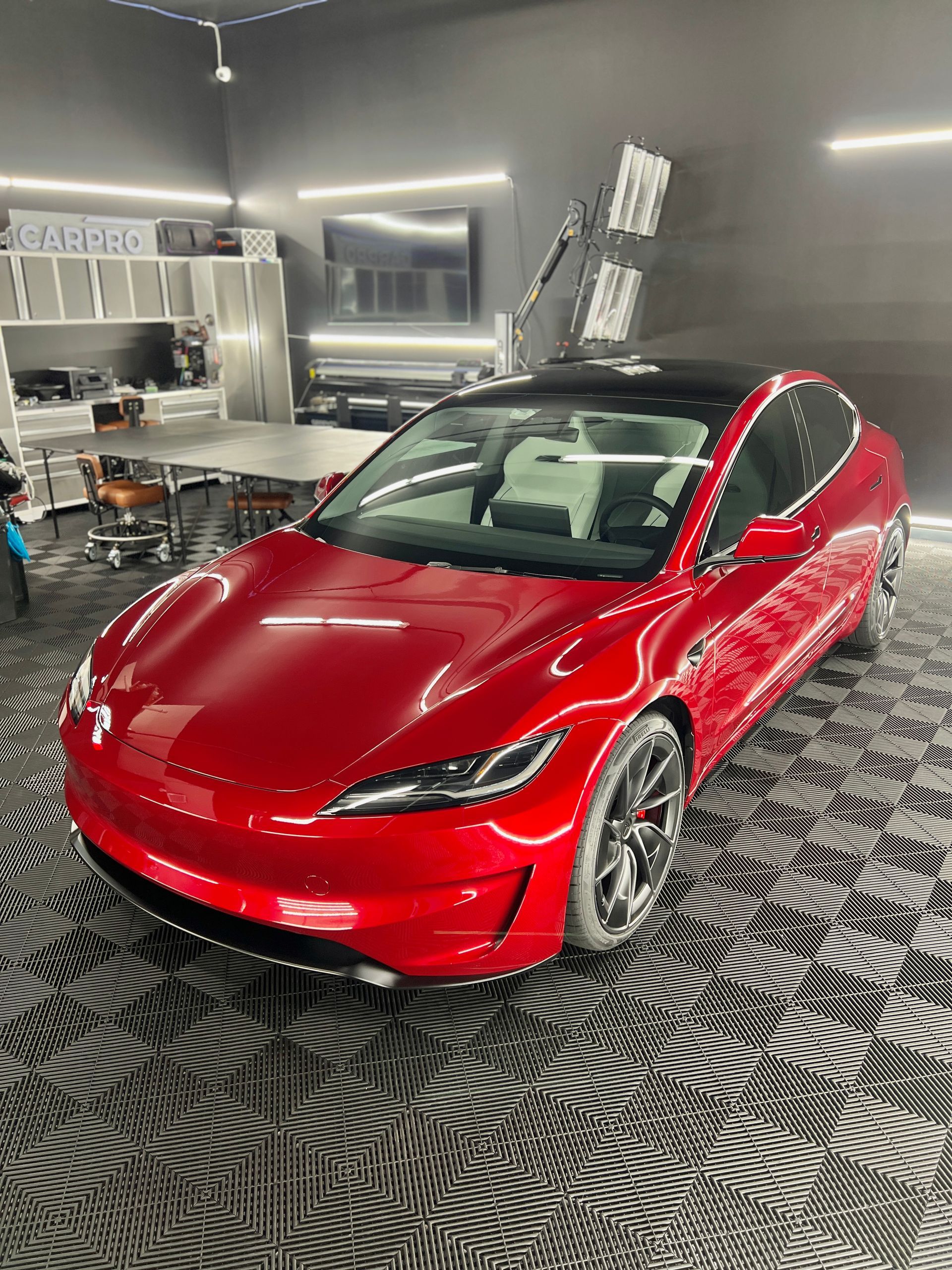 A red tesla model 3 is parked in a garage.