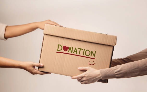 Two people are holding a cardboard box that says donation on it.