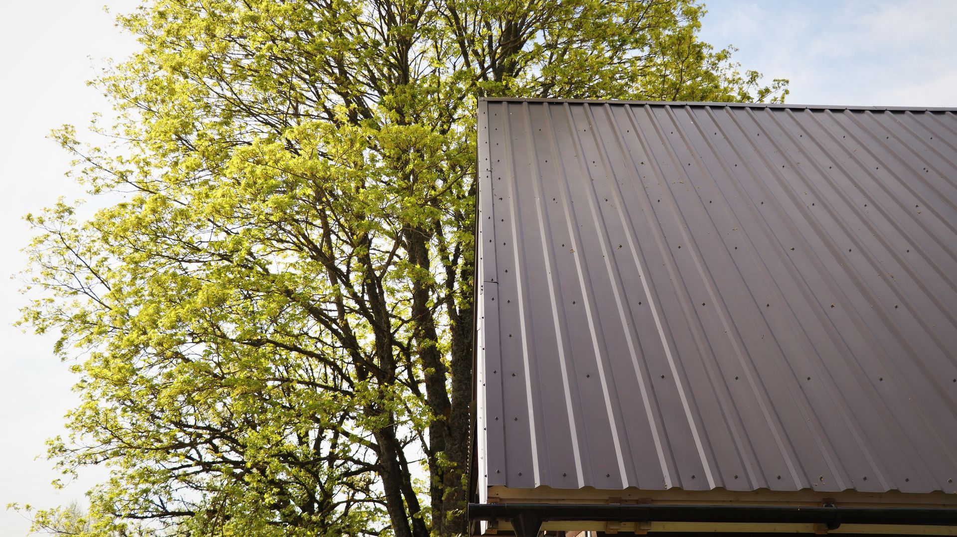 White and dark-grey metal barn with a gravel pile in the foreground under a blue sky.
