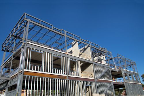 Steel frame of a two-story building under construction against a bright blue sky.