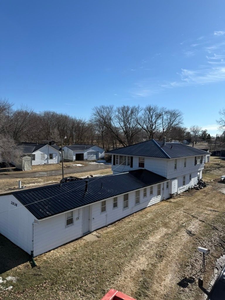 An elevated view of a white two-story building with a long, single-story addition, both featuring dark metal roofs.