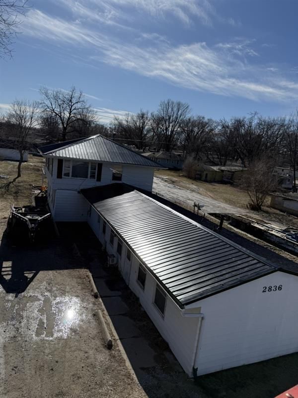 An aerial view of a white, rectangular one-story building with a dark metal roof, set on a bright, sunny day.