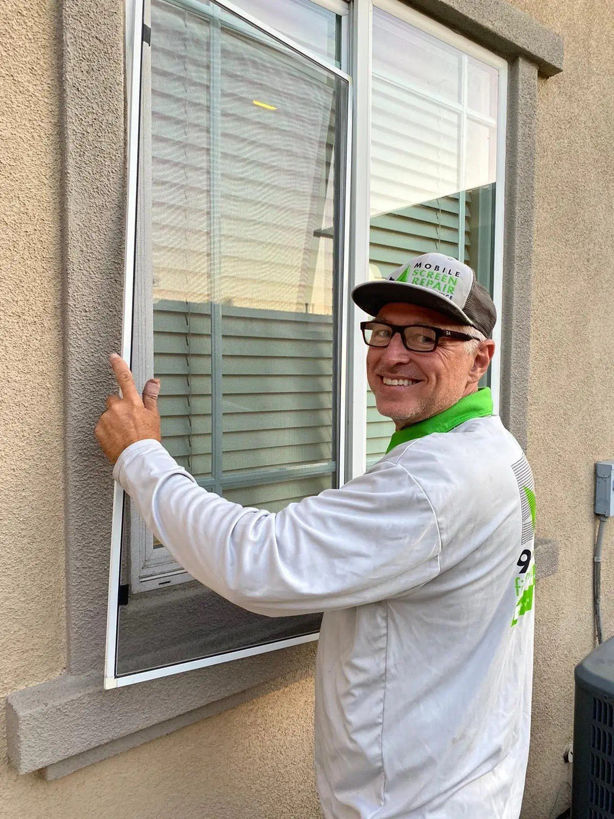 Man installing a window screen on a residential home, securing the frame in place on an exterior window