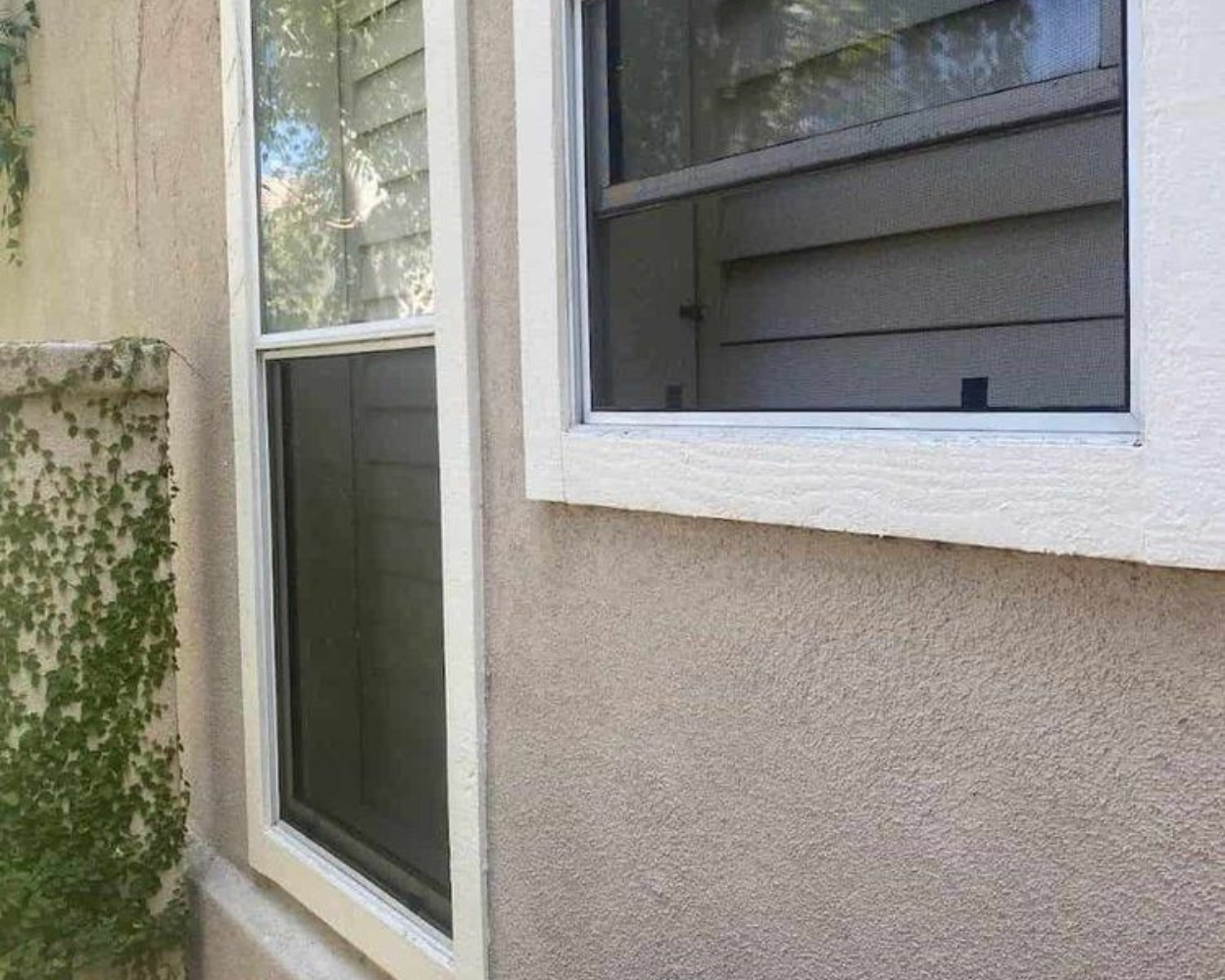 Exterior wall with two windows, a vertical one and a horizontal one, with off-white trim. Light tan stucco siding.