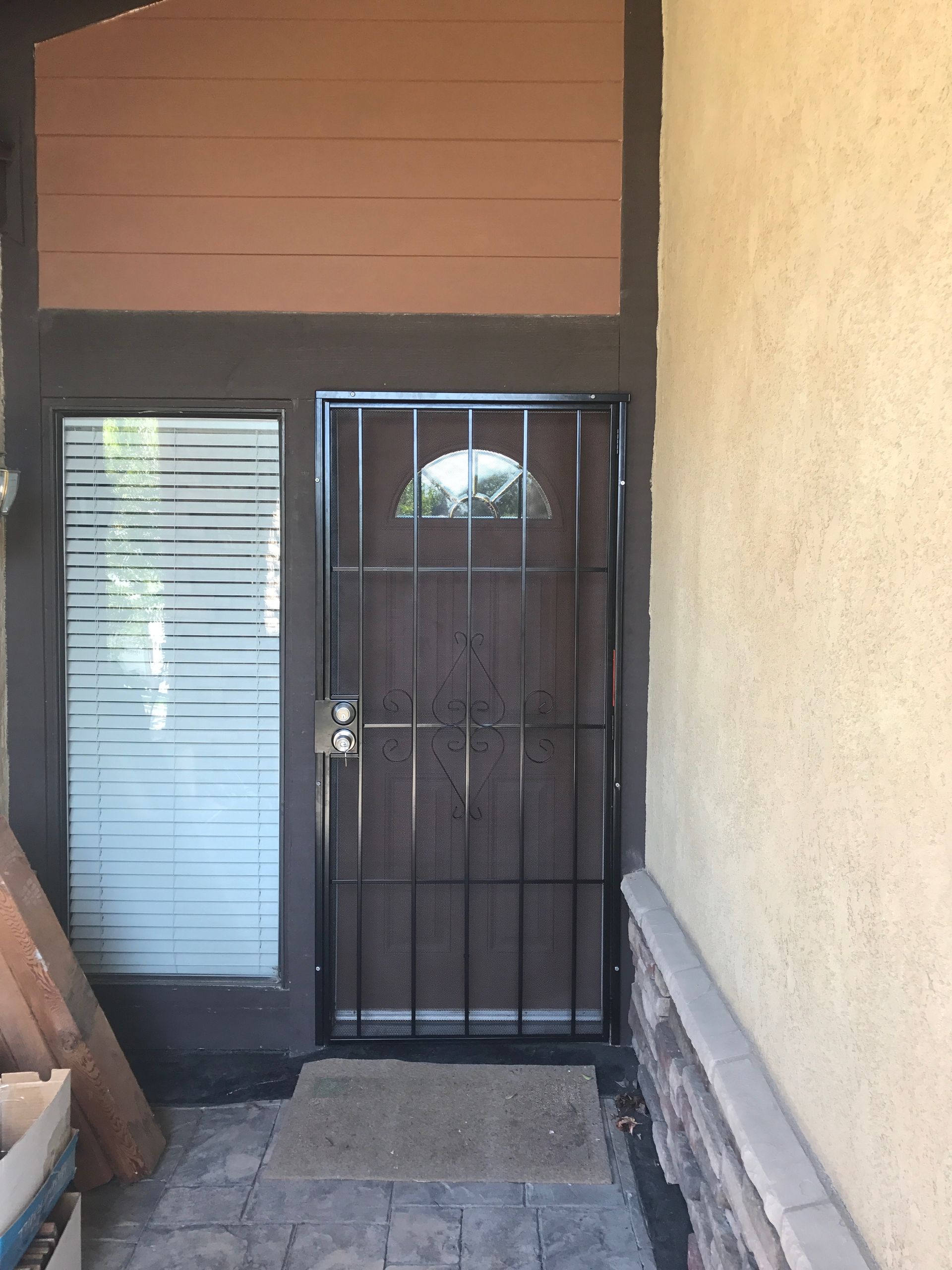 Black metal security door in front of a wood and glass entry. Tan walls and brown trim.