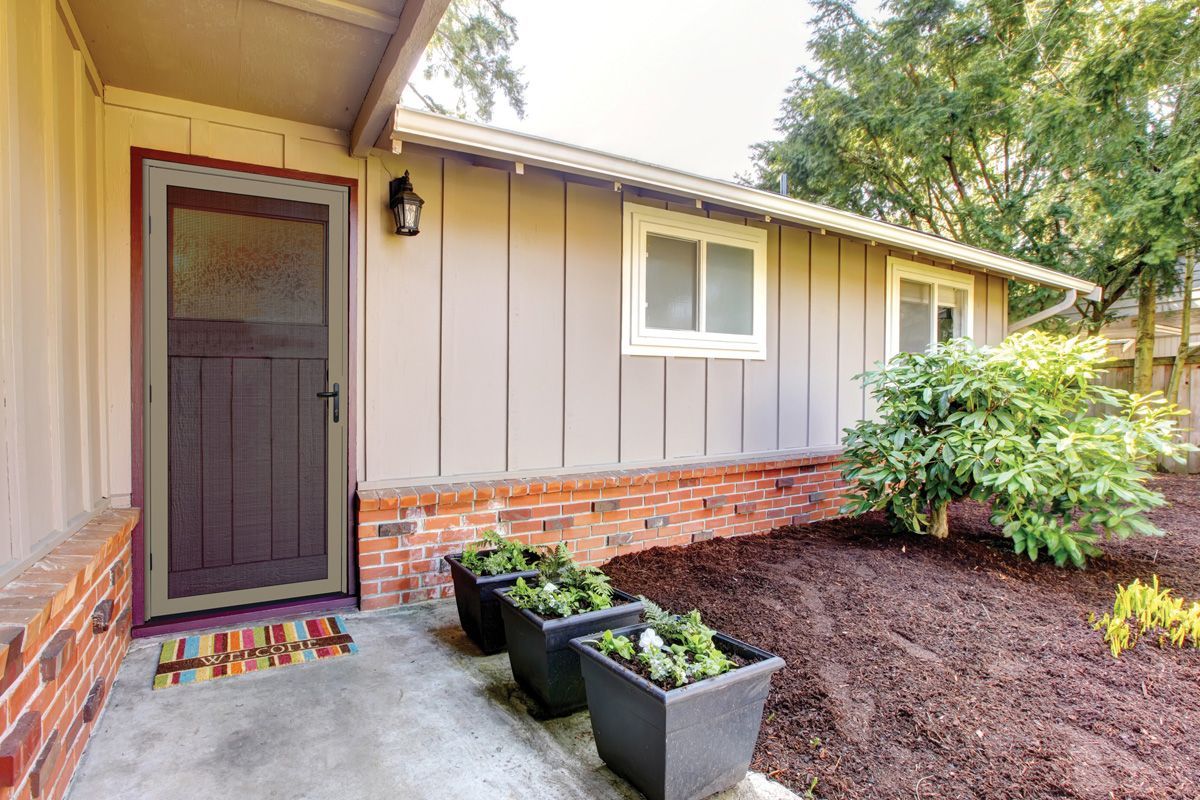 Exterior of a house with a brown door, planters, windows, and landscaping.
