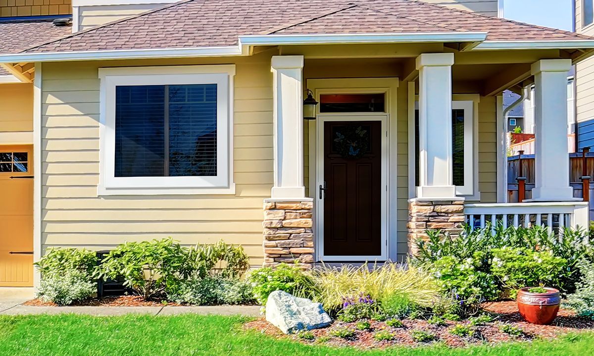 Tan house with a front porch, stone accents, and manicured landscaping.