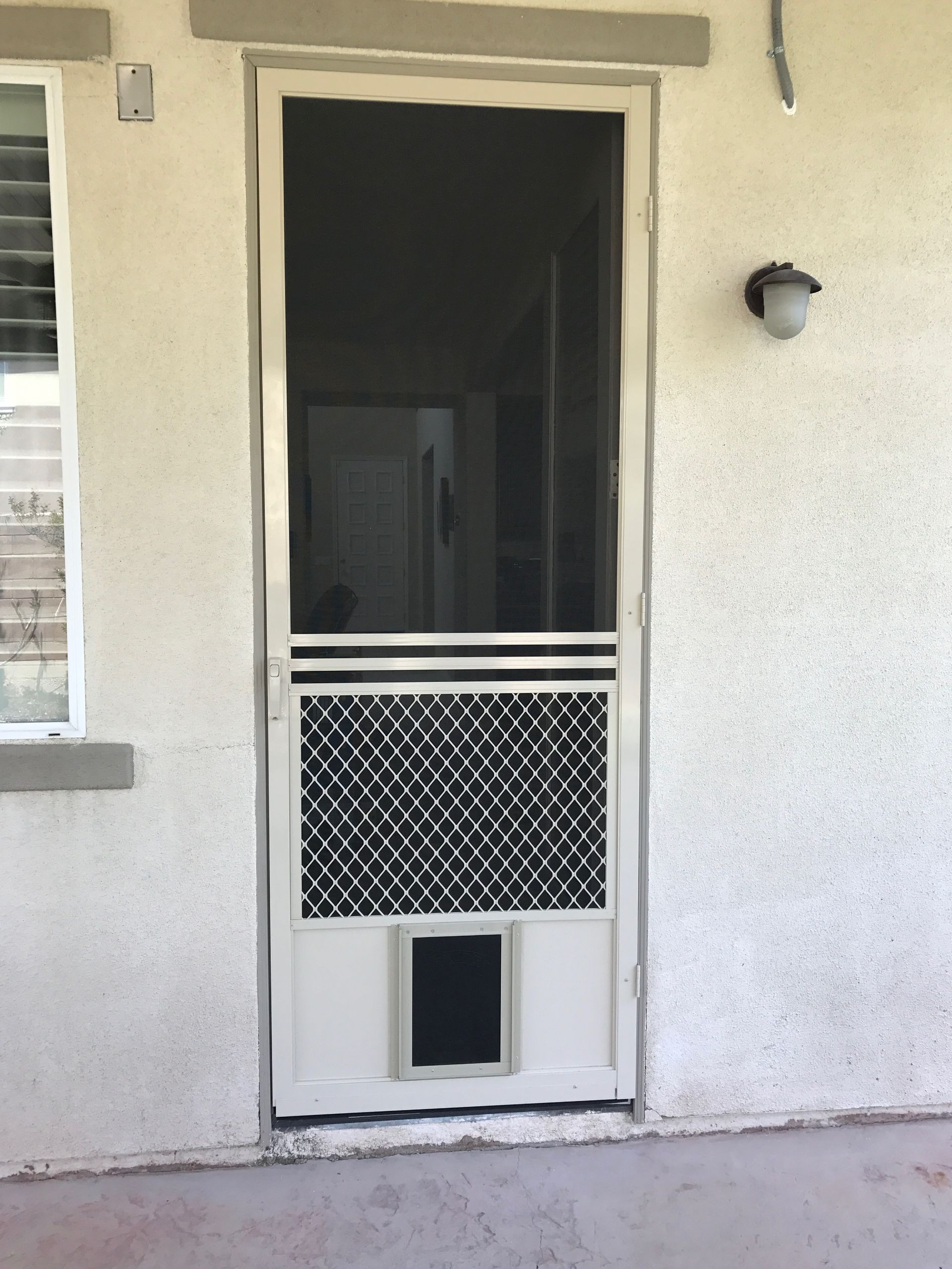 Exterior door with a black security screen door and pet door lower panel