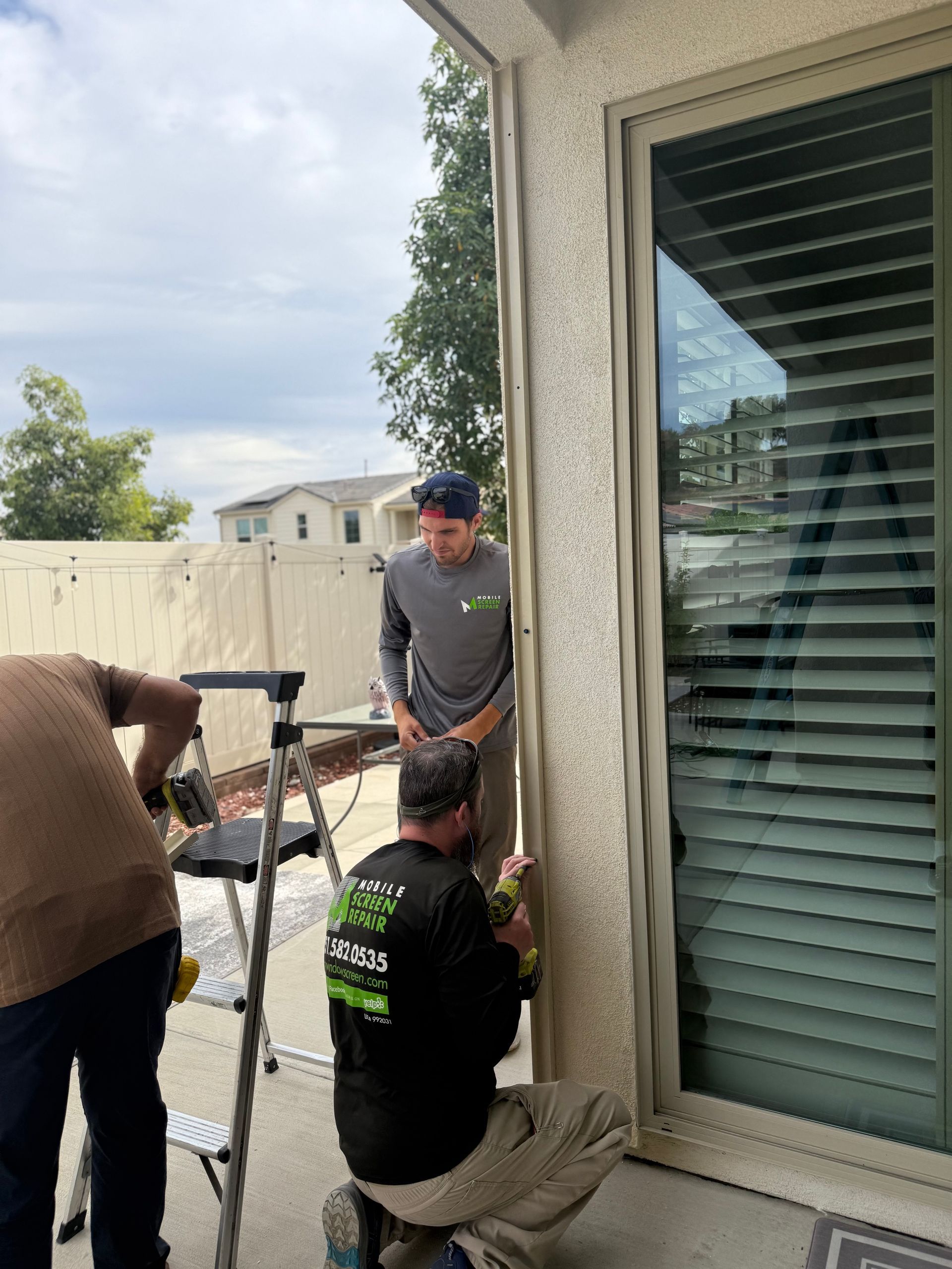 Technician working on a sliding screen door next to a patio window