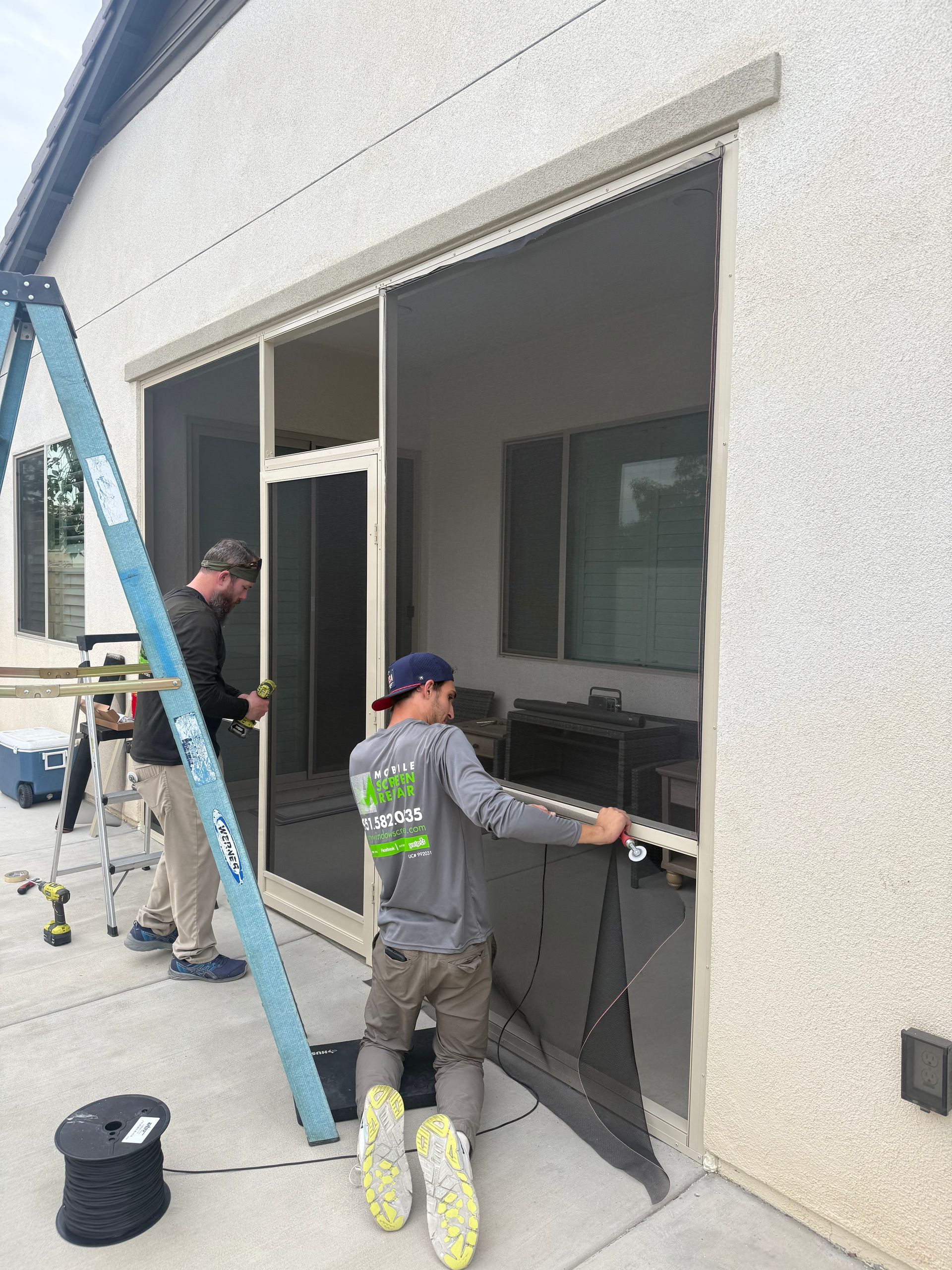 Worker installing or adjusting screen panels on a patio enclosure