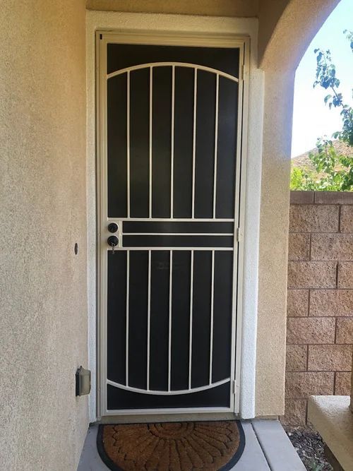 Metal security door with screen and decorative bars, set in a neutral-colored doorway.