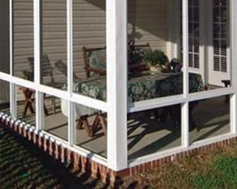 White screened-in porch with brick foundation, housing furniture and a patterned tablecloth.