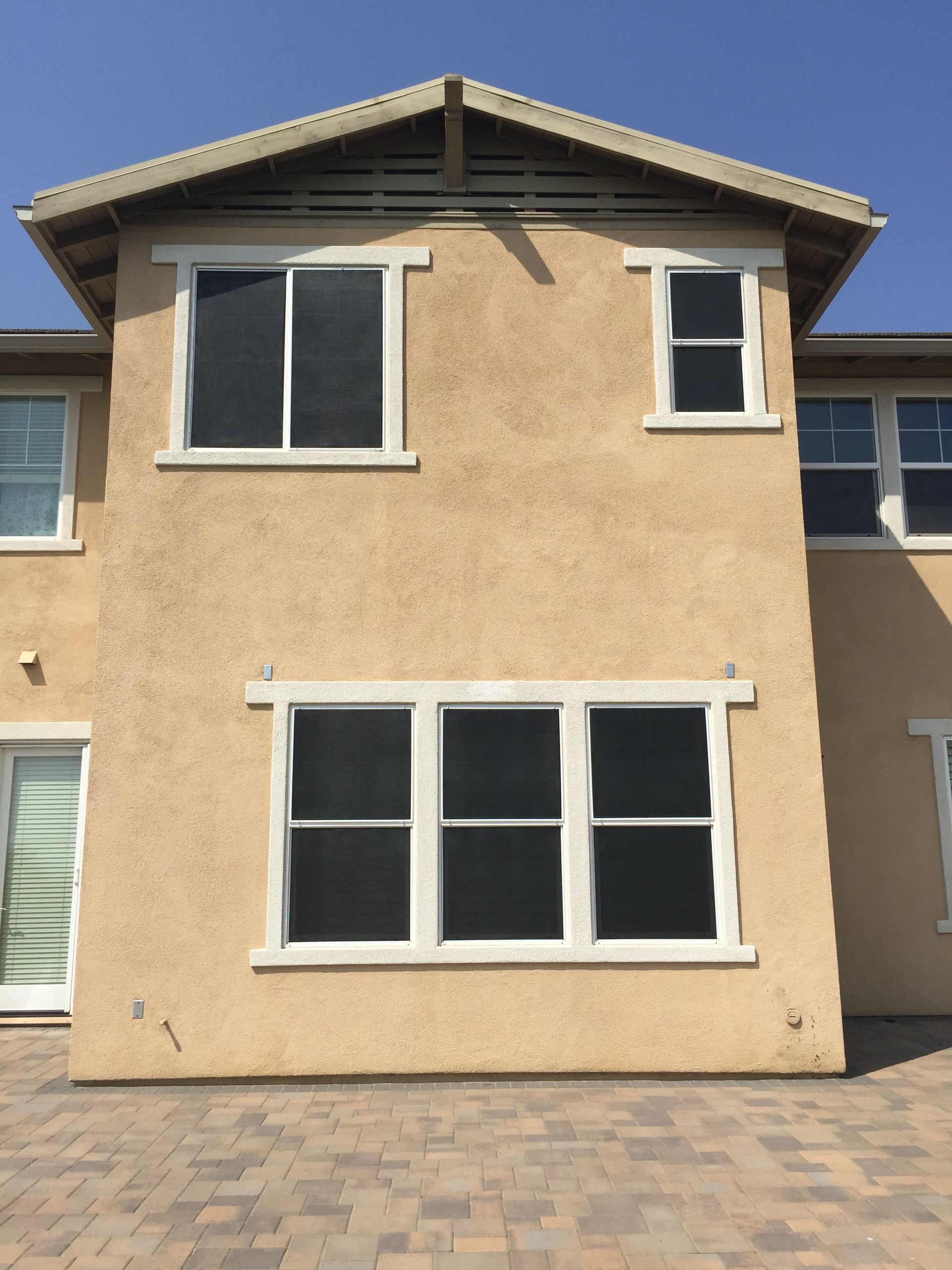 Back exterior of a two-story home with multiple windows fitted with screen mesh above a paved patio area