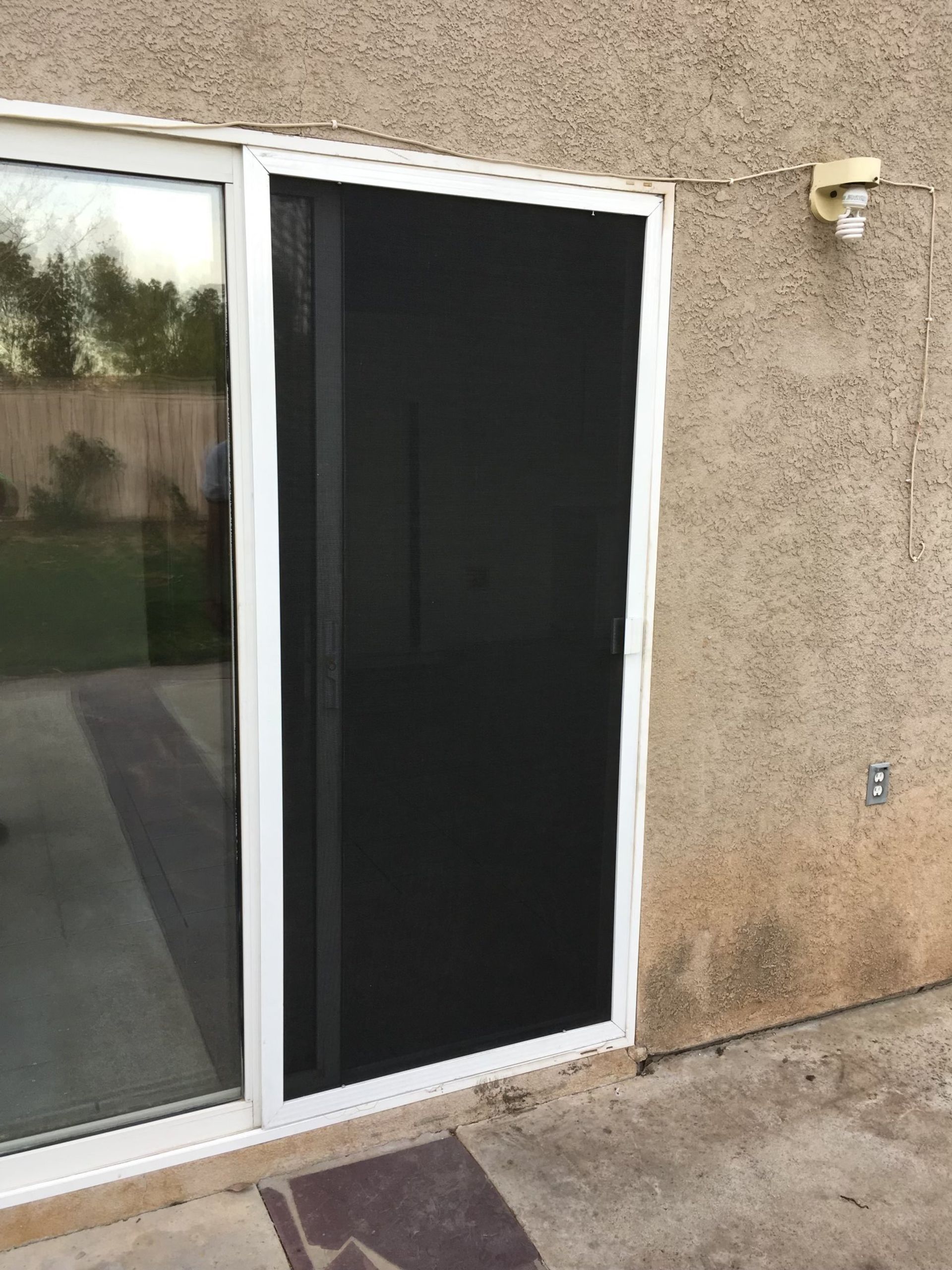 Sliding glass door with a dark screen door on a stucco exterior