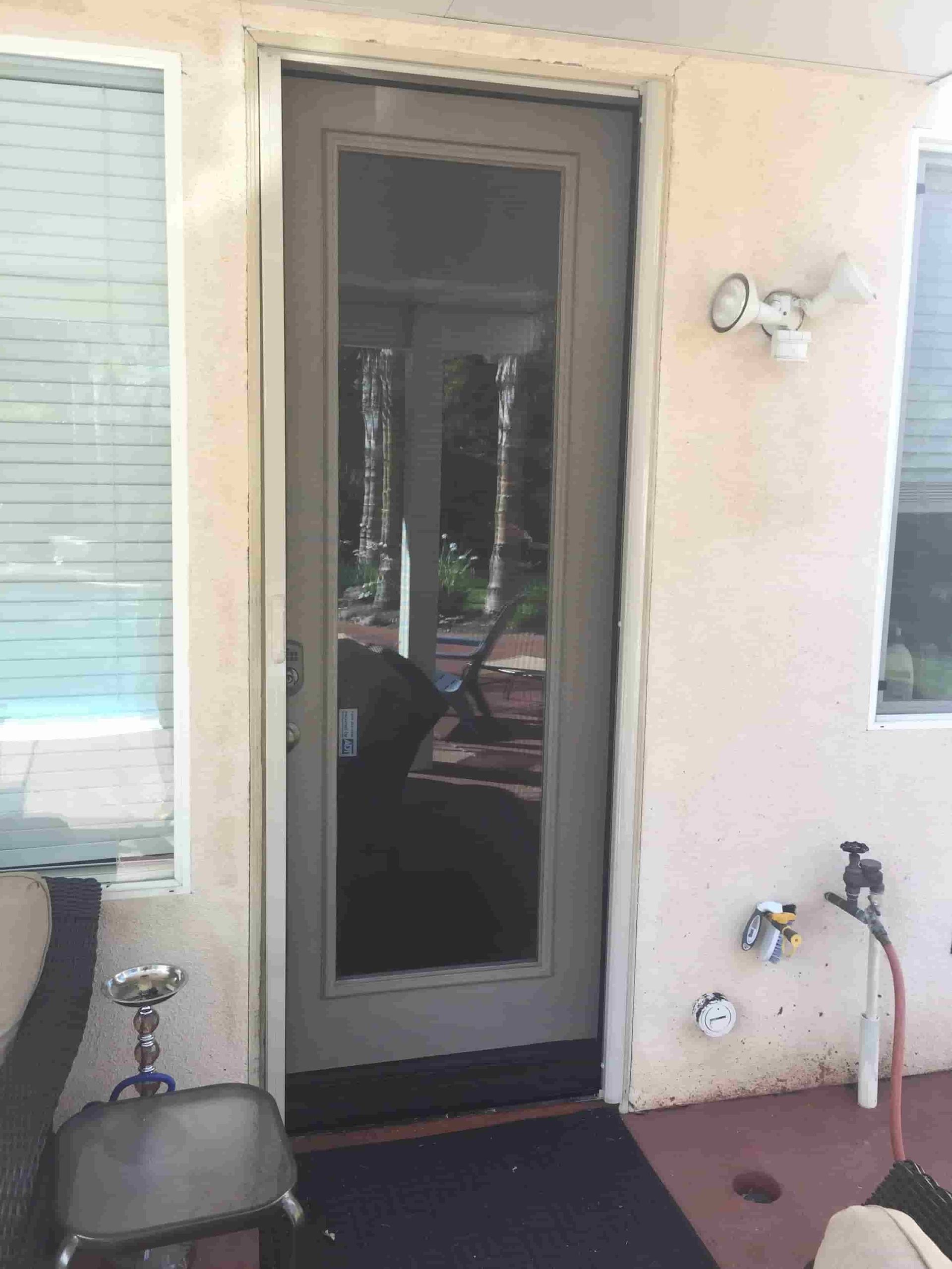Gray door with glass panel on a patio, flanked by windows and a wall with a spigot and light fixture.