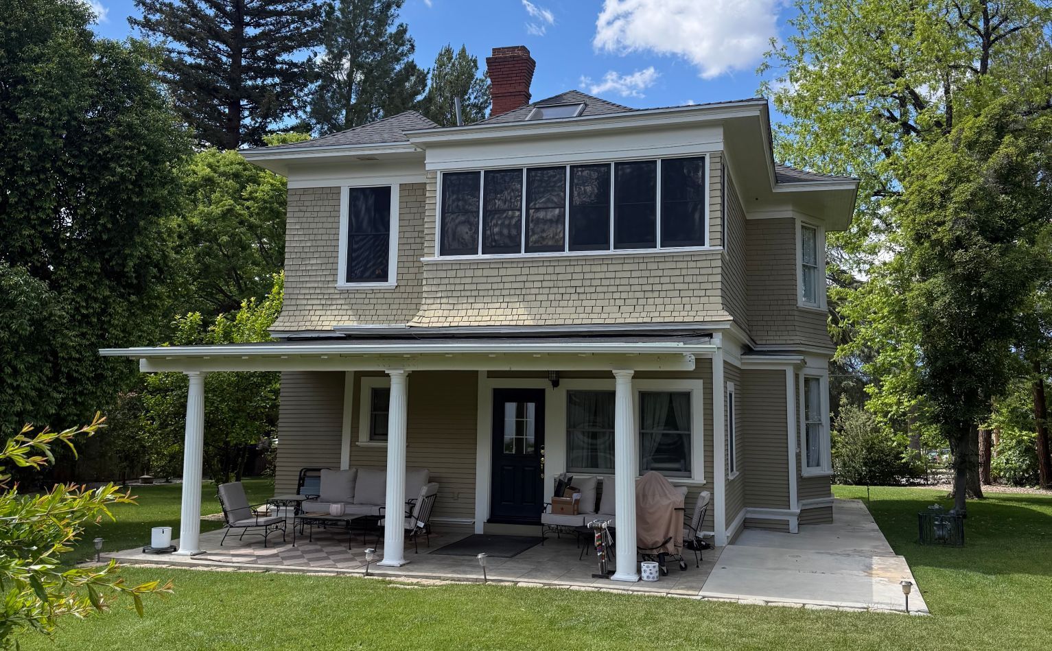 Two-story home with a covered patio and multiple windows fitted with screen enclosures, surrounded by trees and greenery