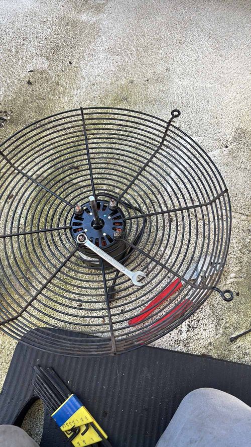 A black metal fan guard with motor, wrench in use, on a black mat outdoors.