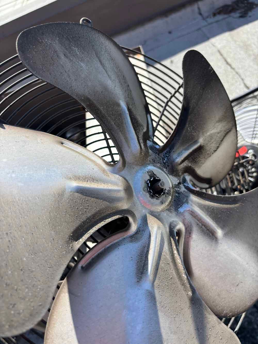 Close-up of a silver fan with four blades, encased in a metal cage, outdoors.