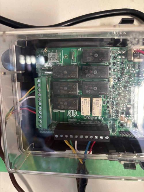 Electronic circuit board inside a clear, plastic enclosure, with several relays, wiring, and terminals.
