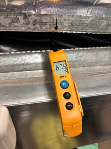 Orange thermometer measuring temperature on metal duct; arrow points to a small opening.