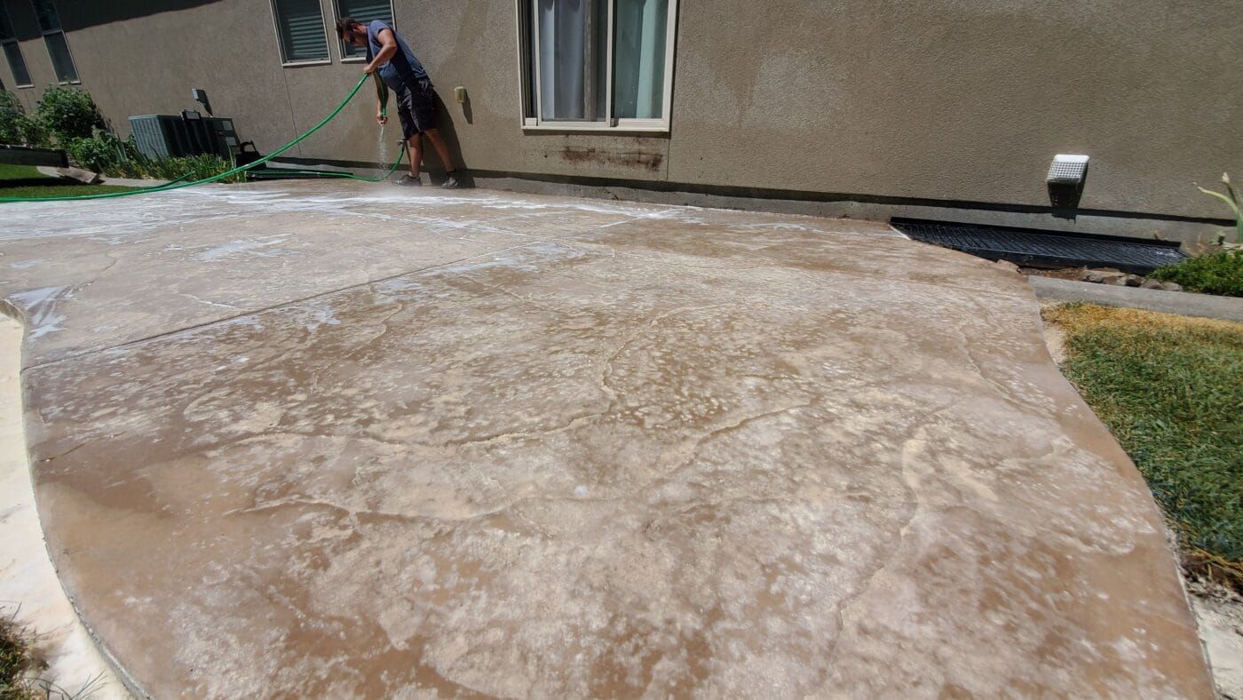 A man is cleaning a concrete patio with a hose.
