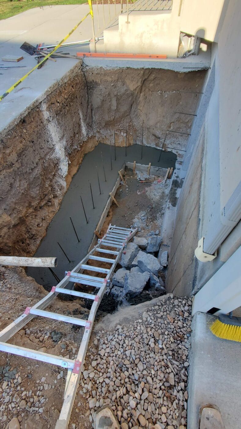 A ladder is sitting in a hole in the ground next to a concrete wall.