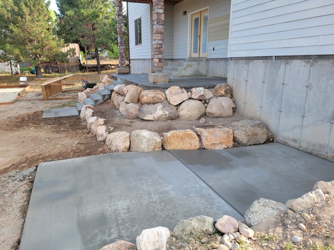 A concrete walkway leading to a house with a stone wall surrounding it.
