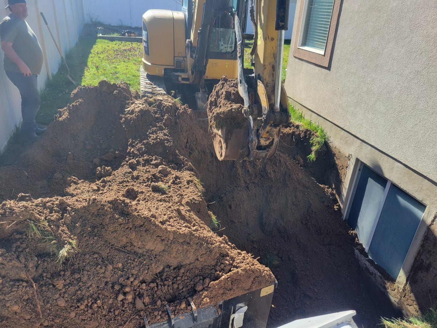 An excavator is digging a hole in the ground in front of a house.
