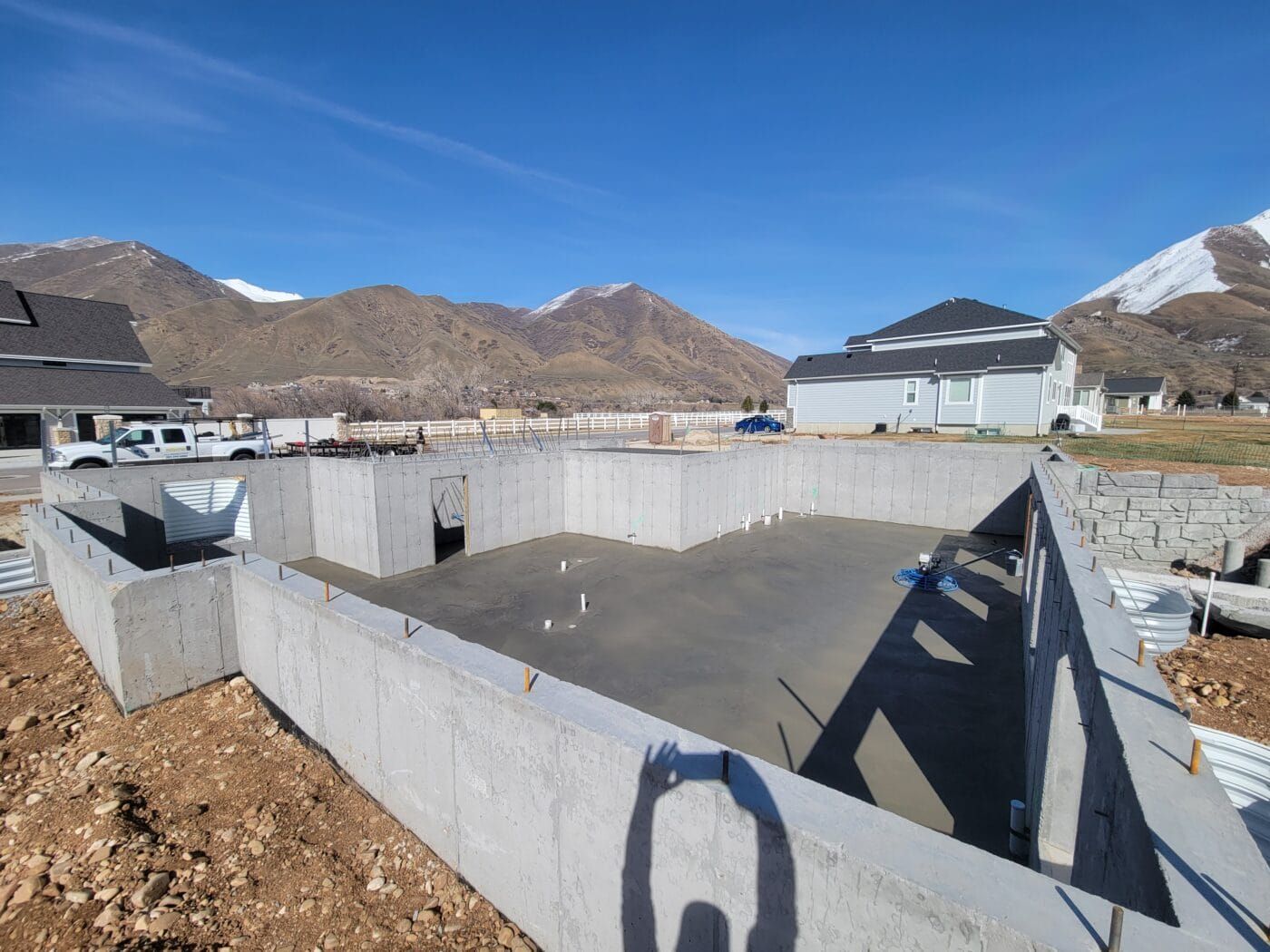 A large concrete wall is surrounding a swimming pool with mountains in the background.