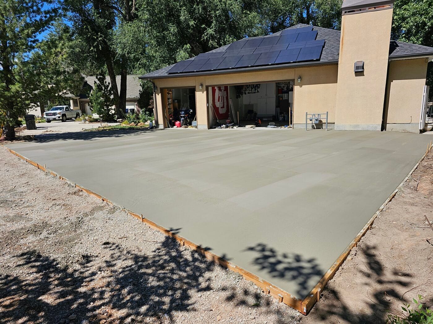 A concrete driveway is being built in front of a house with solar panels on the roof.