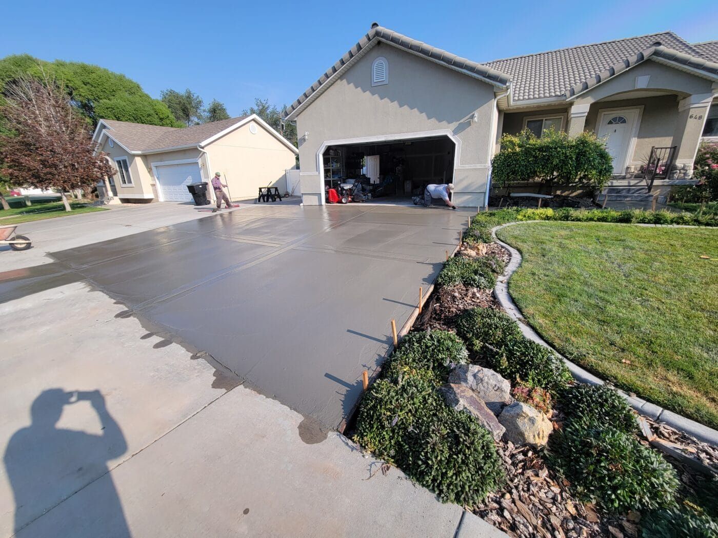 Newly poured concrete driveway in front of a beige house with a detached garage; sunny day.