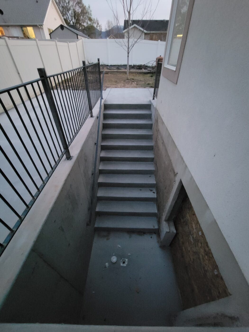 Concrete staircase leading down to a basement door, enclosed by concrete walls and a black railing.