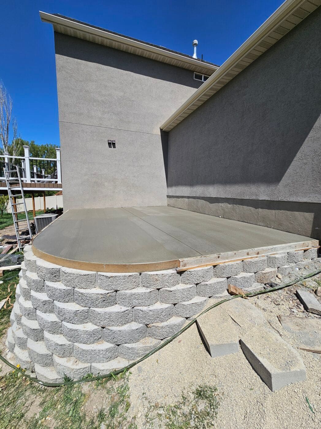 Newly poured concrete patio with a curved edge, supported by a gray retaining wall.