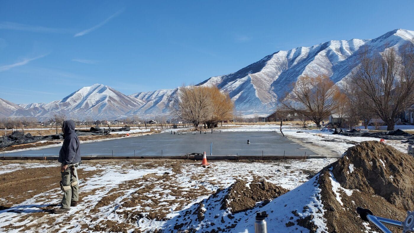 A man is standing in a snowy field with mountains in the background.