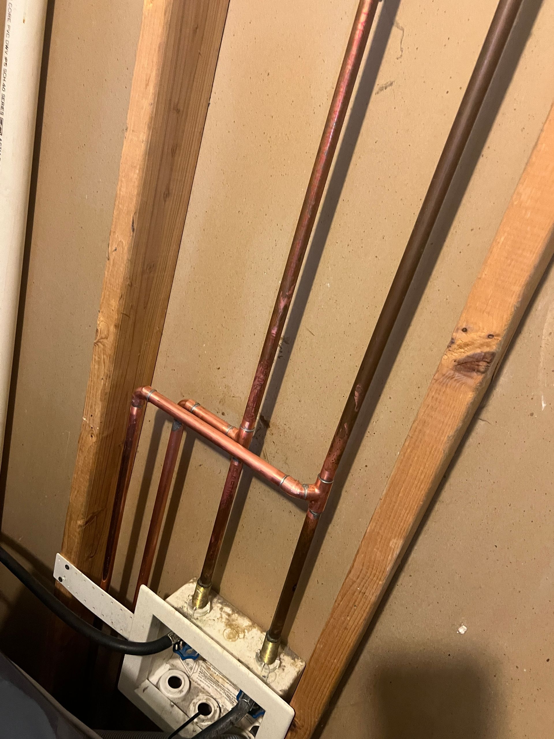 Copper pipes installed within a wooden frame, likely for plumbing.