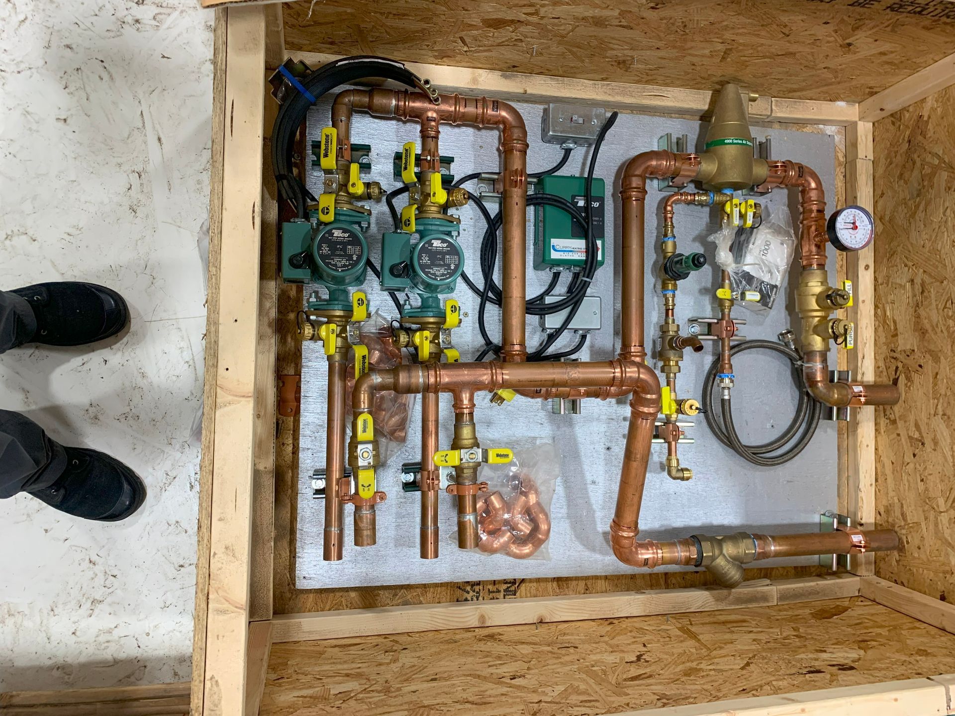 Copper pipes and valves, pumps, and gauges on a panel, inside a wooden box.