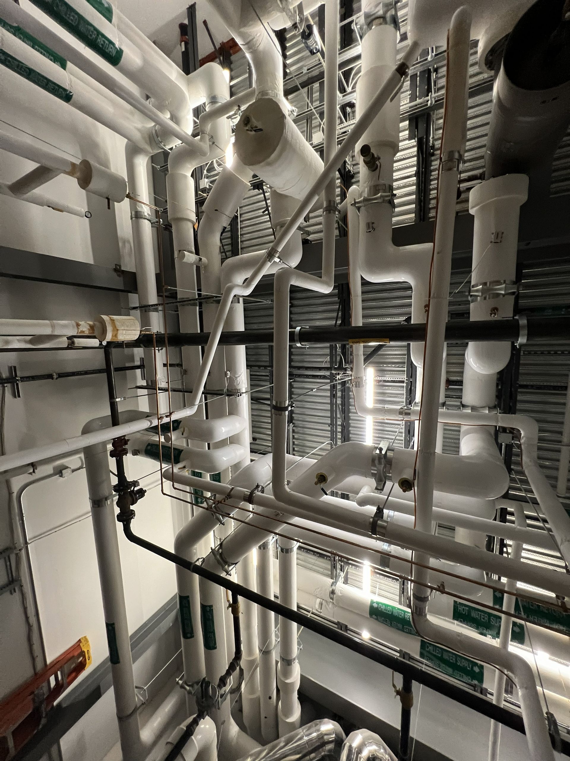 Complex network of white and black pipes and ducts in an industrial setting, with some insulation and valves.