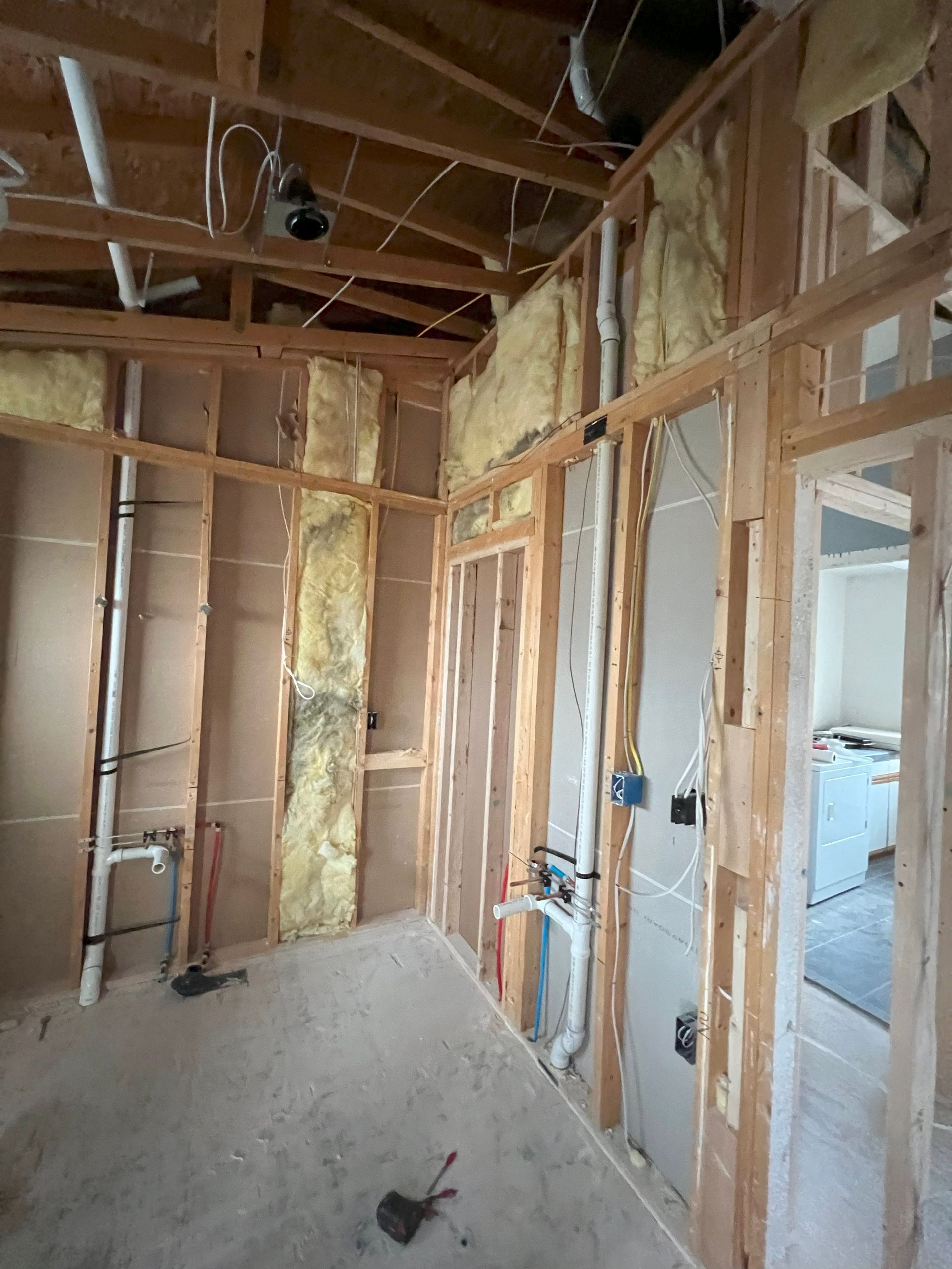 Interior of a room under construction, with exposed wooden framing, insulation, and plumbing.