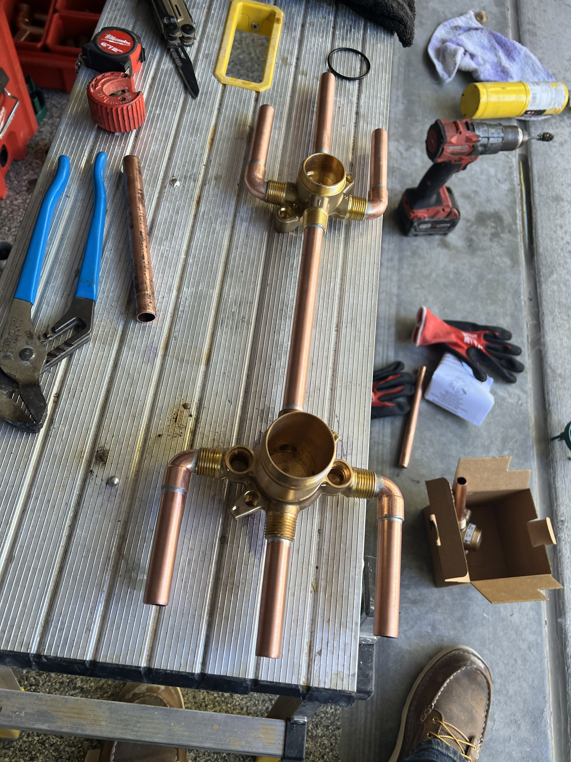 Copper pipe shower valve assembly on a workbench, surrounded by tools and fittings.